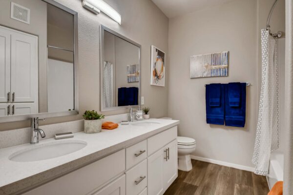 Mandarina apartment bathroom with wood style floor, white cabinets and counters, and dual mirrors.