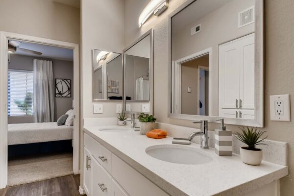 Mandarina apartment bathroom with wood style floor, white cabinets and counters, and dual mirrors.