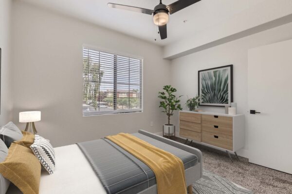 Mandarina apartment bedroom with carpet, plush bed with headboard, dresser with decor, and large window.