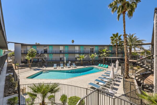 Omnia on Thomas apartments pool area with lounge chairs, umbrellas, and tall palm trees.