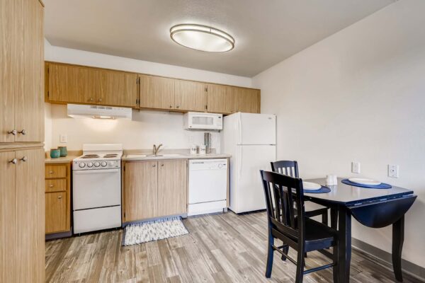 Overlook at Sunset Point apartment kitchen with wood style floor and cabinets, white appliances, and dining table.