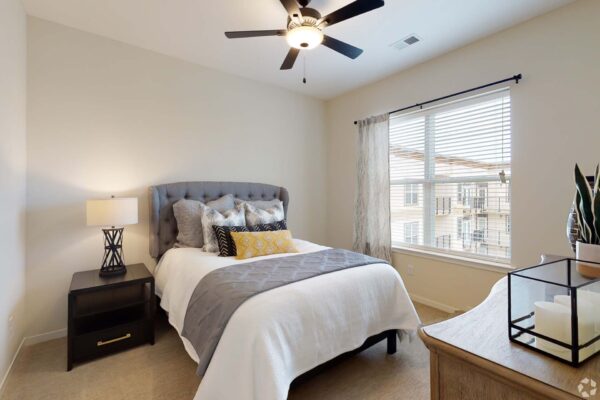 The Locale apartment bedroom with carpet, plush bed with headboard, and ceiling fan.