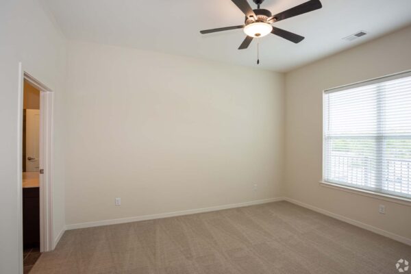 The Locale apartment bedroom with carpet, large window, and ceiling fan.