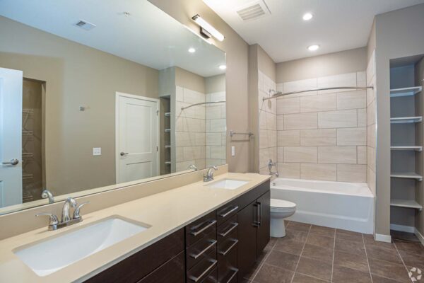 The Locale apartment bathroom with tile, dark cabinets, large mirror, and tiled shower tub.