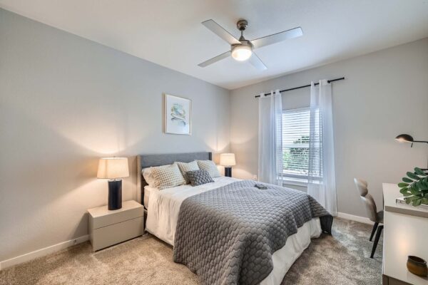 The Avery apartment bedroom with carpet, plush bed with headboard, desk, and large window.
