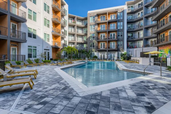 Arte St. Pete apartments pool area with lounge chairs, umbrellas, palm trees, and apartment balconies.