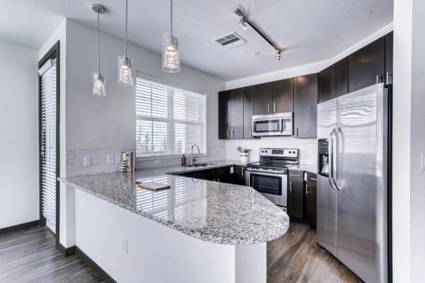 Centre Court apartment kitchen with wood style floor and cabinets, stone counters, and stainless steel appliances.