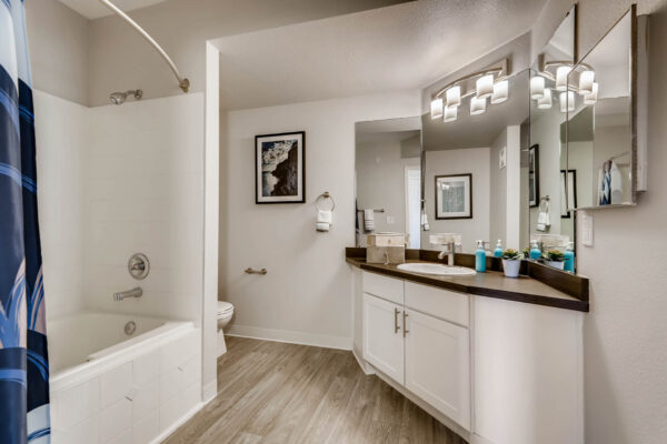 Copper Ridge apartment bathroom with wood style floor, white cabinets, triple mirror, and tiled shower tub.