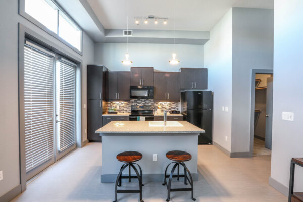 Forum Fitzsimons apartment kitchen with wood style floor, dark cabinets, and black appliances.
