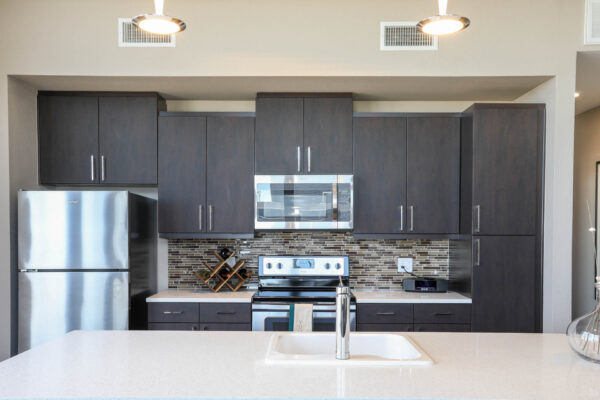 Forum Fitzsimons apartment kitchen with wood style cabinets, light counters, and stainless steel appliances.