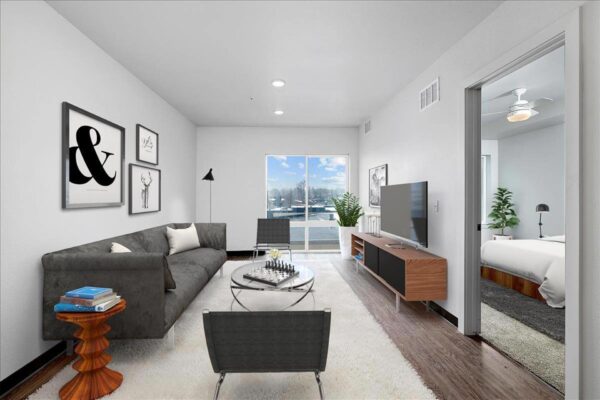 The Overland apartment living room with plush seating, console with TV, wall art, and large windows.