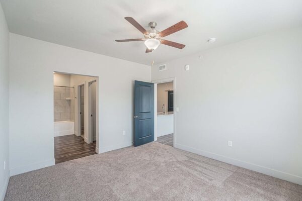 The Marc at Monument Ridge apartment bedroom with plush carpet, ceiling fan, and bathroom entry.
