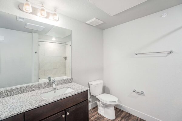 The Marc at Monument Ridge apartment bathroom with wood cabinets, stone counters, and large mirror.