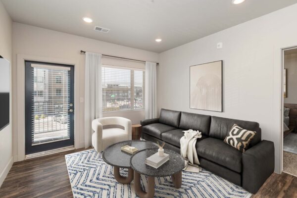 The Marc at Monument Ridge apartment living room with plush couch, wall mounted TV, and balcony door.