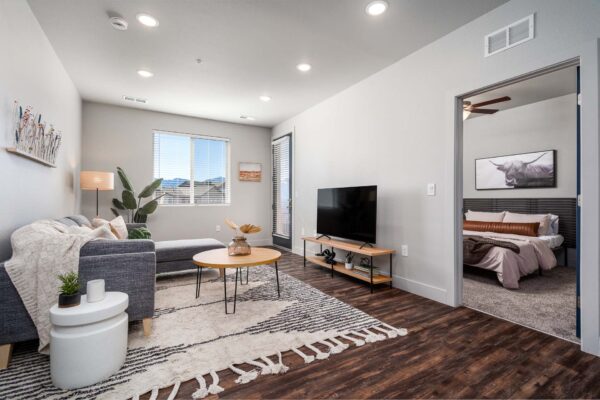 The Flats at Aero Park apartment living room with wood style floor, plush couch, console with TV, and balcony door.