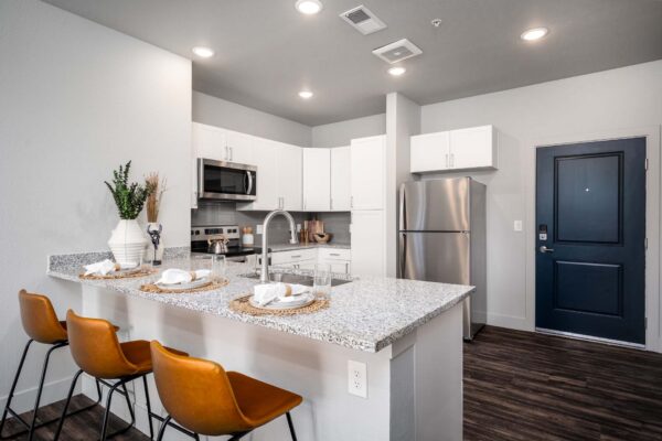 The Flats at Aero Park apartment kitchen with wood style floor, breakfast bar with stools, and stainless steel appliances.