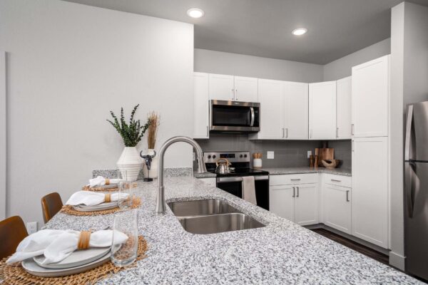 The Flats at Aero Parks apartment kitchen with stone counters, white cabinets, and stainless steel appliances.