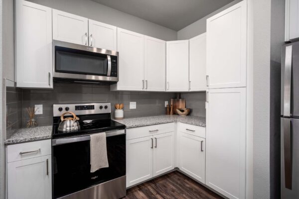 The Flats at Aero Park apartment kitchen with wood style floor, white cabinets, and stainless steel appliances.