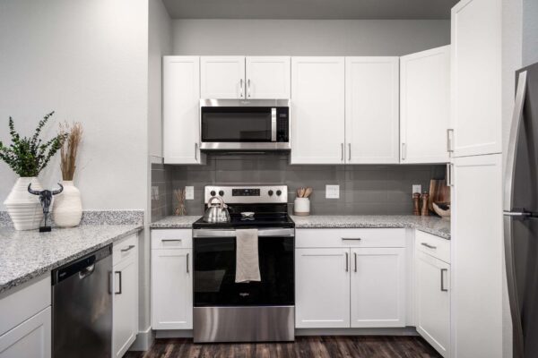 The Flats at Aero Park apartment kitchen with wood style floor, white cabinets, and stainless steel appliances.