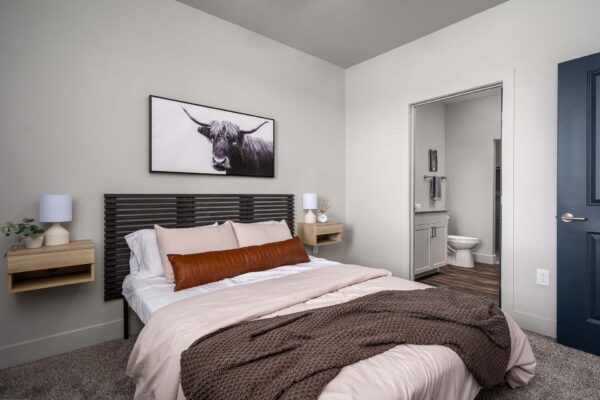 The Flats at Aero Park apartment bedroom with carpet, plush bed with headboard, ceiling fan, and bathroom door.