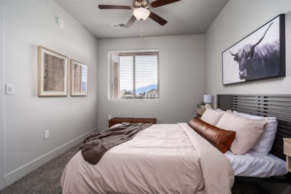 The Flats at Aero Park apartment bedroom with carpet, plush bed with headboard, ceiling fan, and large window.
