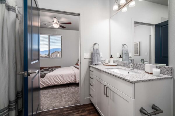 The Flats at Aero Park apartment bathroom with wood style floor, white cabinets, stone counters, and large mirror.