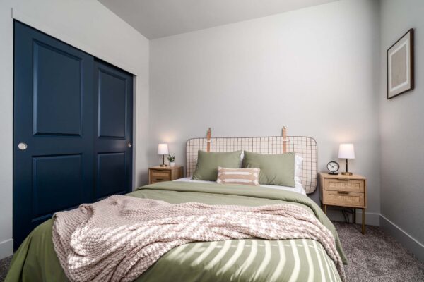 The Flats at Aero Park apartment bedroom with carpet, plush bed with headboard, and bedside tables with lamps.