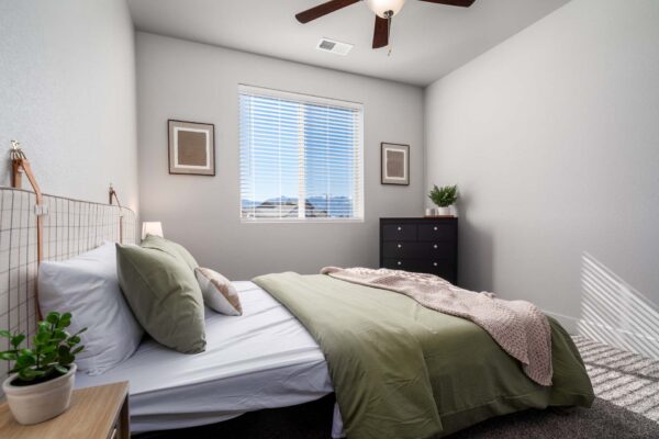 The Flats at Aero Park apartment bedroom with carpet, plush bed with headboard, and dresser.