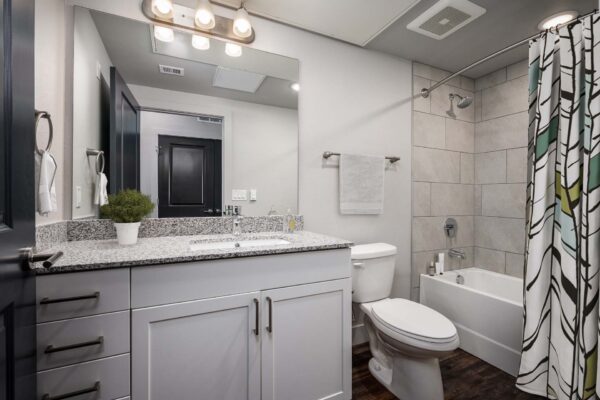The Flats at Aero Park apartment bathroom with white cabinets, stone counters, and tiled shower tub with curtain.