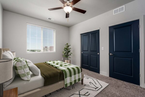 The Flats at Aero Park apartment bedroom with carpet, plush bed, ceiling fan, and large windows.