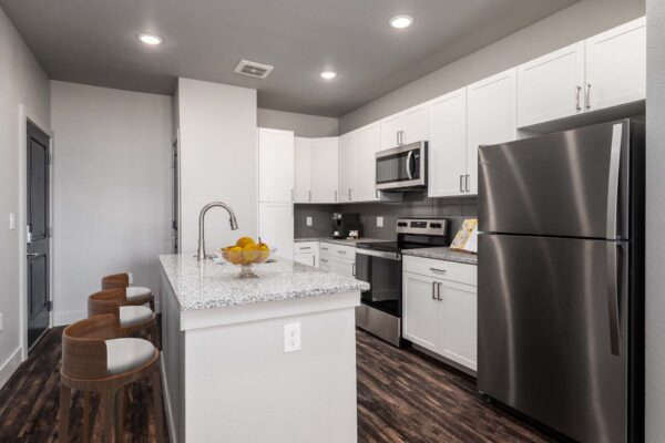 The Flats at Aero Park apartment kitchen with wood style floor, white cabinets, stone counters, and stainless steel appliances.