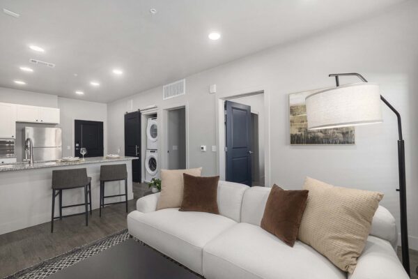 The Preserve at Mesa Creek apartment living room with wood style floor, plush couch, and kitchen with breakfast bar.