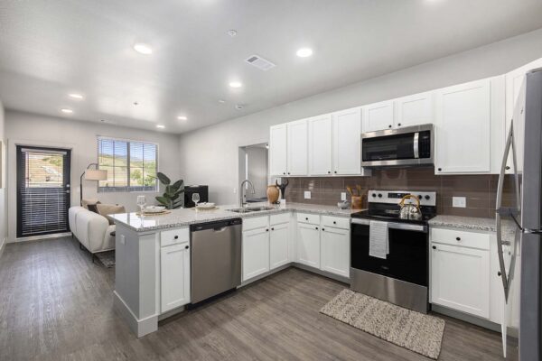The Preserve at Mesa Creek apartment kitchen with wood style floor, white cabinets, stone counters, and stainless steel appliances.