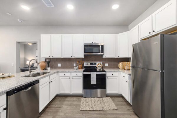 The Preserve at Mesa Creek apartment kitchen with wood style floor, white cabinets, stone counters, and stainless steel appliances.