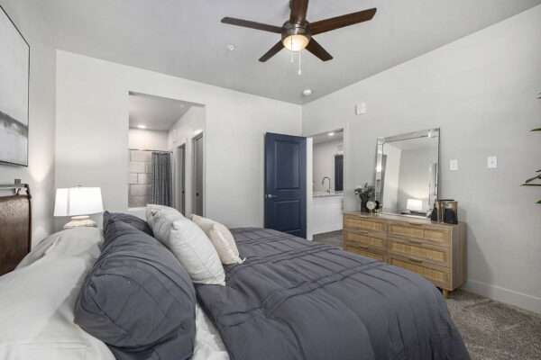 The Preserve at Mesa Creek apartment bedroom with carpet, plush bed, dresser, and ceiling fan.