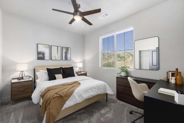 The Preserve at Mesa Creek apartment bedroom with carpet, plush bed with headboard, desk with chair, and large window.